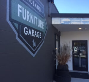 A building exterior with a large "Furniture Garage" sign painted on the wall and a planter made from stacked tires.