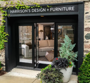Storefront of Harrison's Design + Furniture with glass doors revealing a modern sofa and decor inside, plants by the entrance.