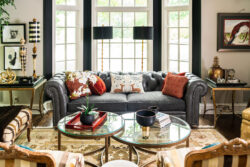 A stylish living room with a gray tufted sofa, glass tables, art decor, and large windows letting in natural light.