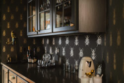 A kitchen counter with appliances, glassware, and cabinets against bug-patterned wallpaper.