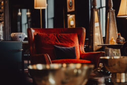A red velvet armchair with pillows sits in a warmly lit, upscale living room with decorative lamps and art.