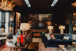 Eclectic living room with dark walls, vintage decor, blue velvet sofa, and large cityscape artwork on the back wall.
