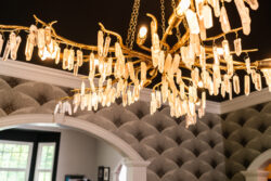 A gold chandelier with crystal accents hangs from the ceiling in a room with patterned wallpaper and arched doorways.