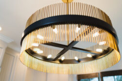 Close-up of a modern circular chandelier with gold vertical rods and exposed lightbulbs, hanging from a ceiling.