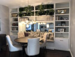A dining area with a round table, four upholstered chairs, built-in shelves, and a modern chandelier.