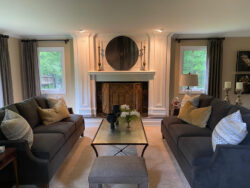 A living room with two gray sofas facing a glass coffee table and a fireplace with a circular wall decor above.